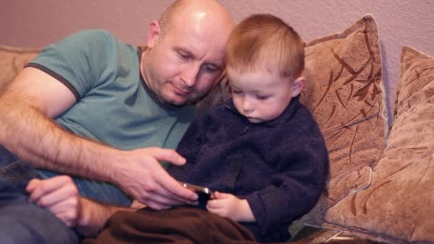 Kleine jongen met zijn oom lettend op een film op uw telefoon — Stockvideo