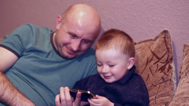 Kleine jongen met zijn oom lettend op een film op uw telefoon — Stockvideo