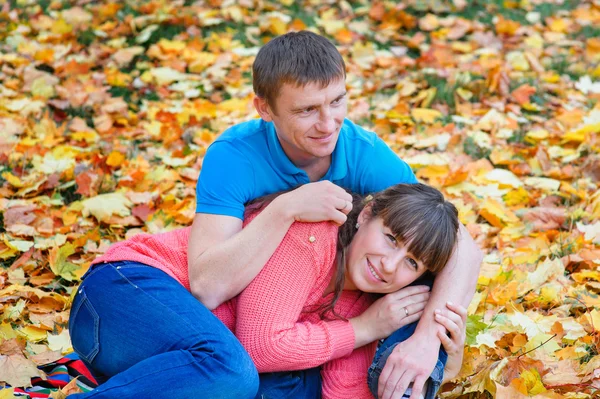 Embracing young couple sitting in a park on yellow leaves in aut — Stock Photo, Image