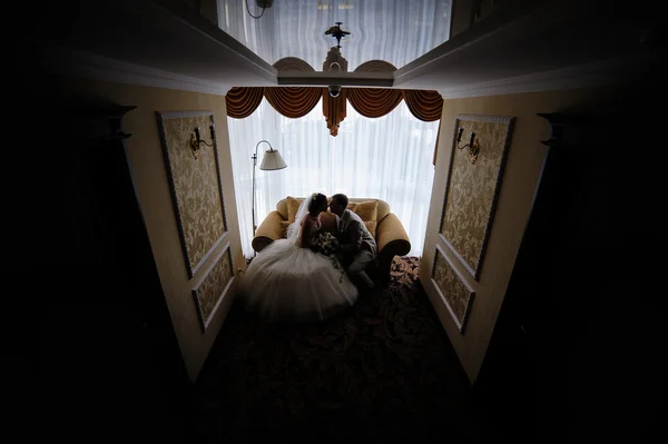 Silhouette of bride and groom sitting on the couch in the room — Stock Photo, Image