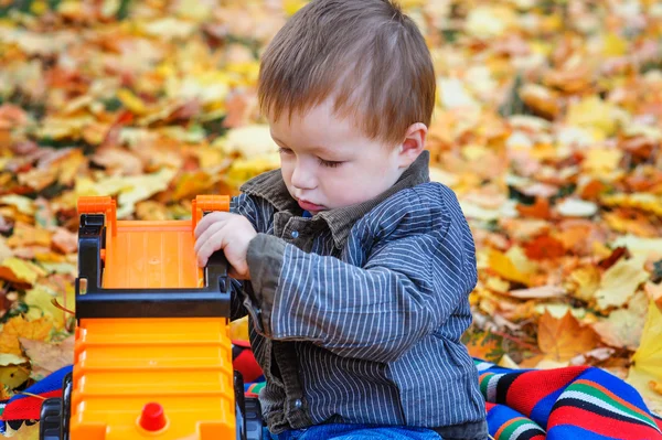 Мальчик играет с автоматом в парке на жёлтых листьях — стоковое фото