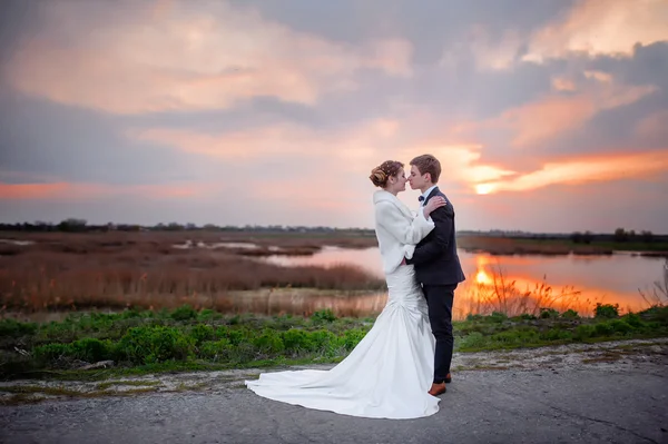 Novia y novio cerca del lago por la noche al atardecer —  Fotos de Stock