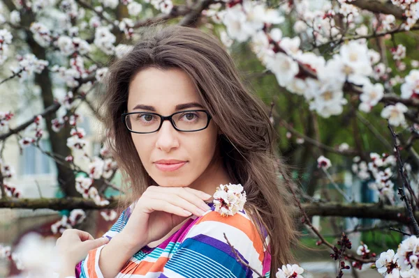 Belle femme en lunettes sur un fond d'arbre en fleurs — Photo