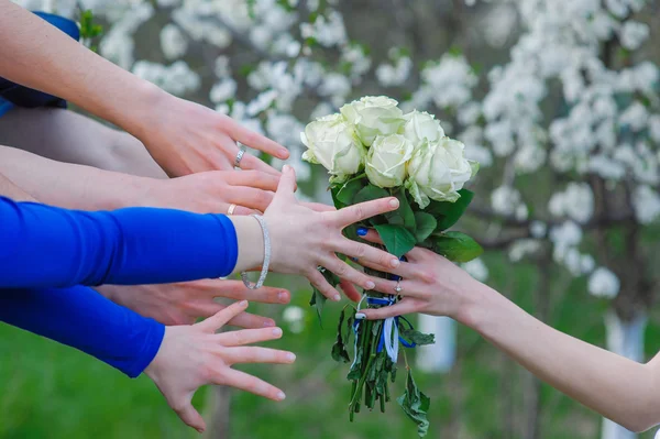 bride holds a wedding bouquet and many hands reach for him