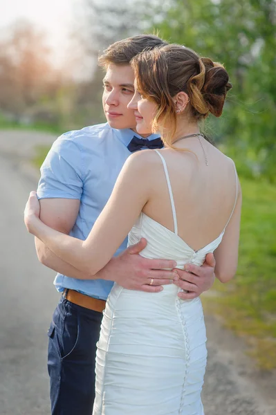 Bruden och brudgummen kramas på vägen under våren — Stockfoto