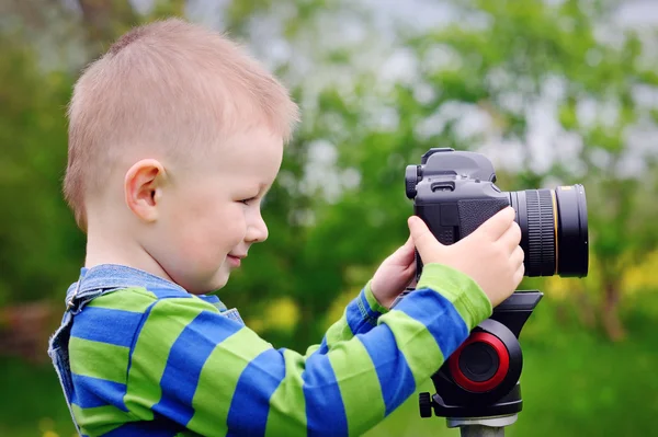 Rapaz bonito atirando com câmera no prado na primavera — Fotografia de Stock