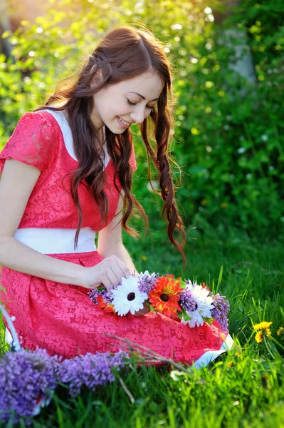 Vacker kvinna i röd klänning gör en krans av blommor — Stockfoto