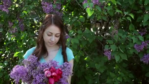 Hermosa mujer caminando en el parque de primavera con un ramo de lila — Vídeos de Stock
