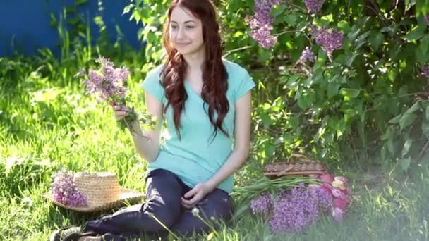 Vacker kvinna med en bukett av lila sitter i parken våren på gräset — Stockvideo