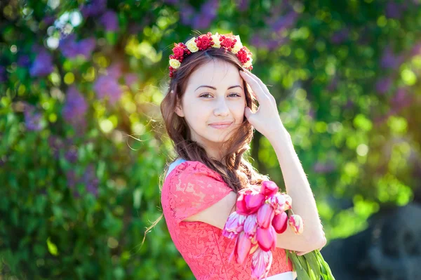 美丽的年轻女子用花圈花在花园里散步 — 图库照片