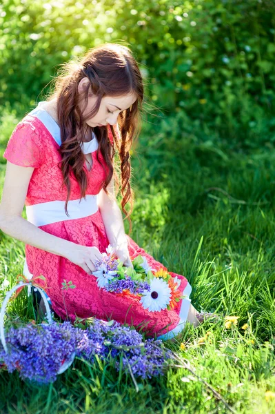 Beautiful woman in red dress sitting on the grass with a branch of lilac — Stock Photo, Image