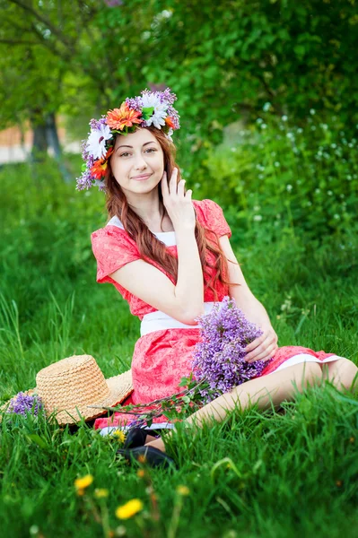 Hermosa mujer en vestido rojo sentado en la hierba con una rama de lila — Foto de Stock