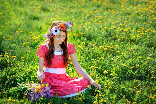 Mulher bonita em vestido vermelho sentado na grama com um ramo de lilás — Fotografia de Stock