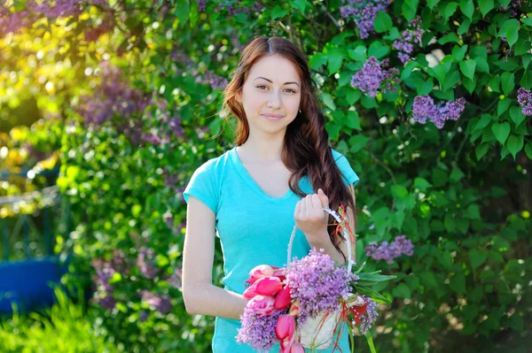 Krásná žena s kytici šeříku a tulipány chůzi v zahradě — Stock fotografie