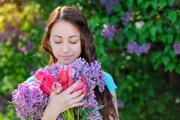 美丽的女子和一束紫丁香和郁金香在花园里散步 — 图库照片