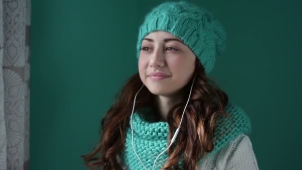 Красивая девушка в вязаной шляпе слушает музыку в наушниках — стоковое видео