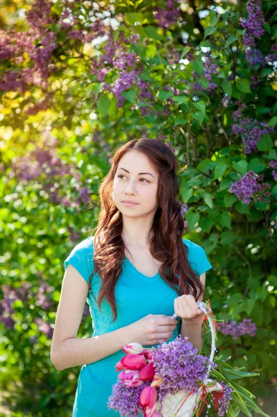 Belle femme marchant dans le jardin de printemps avec un panier de fleurs — Photo