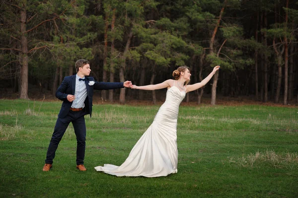 Glückliche Braut und Bräutigam beim Spaziergang am Rande eines Kiefernwaldes im Frühling — Stockfoto