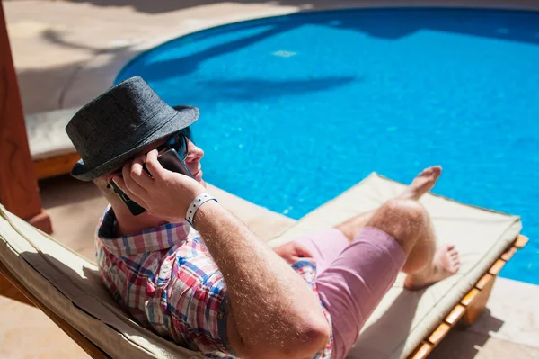 Homme dans un chapeau assis près de la piscine et parlant au téléphone — Photo