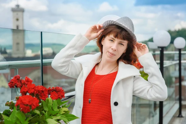 Schöne Frau in einem weißen Mantel in der Nähe der roten Blumen im Hintergrund lviv — Stockfoto