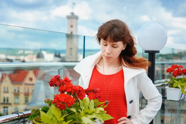 Krásná žena v bílém plášti nedaleko červené květy na pozadí Lvov — Stock fotografie