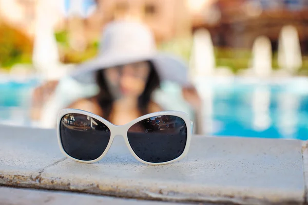 Sunglasses in the foreground and the background is blurred woman in the pool — Stock Photo, Image