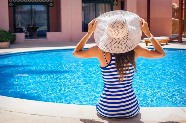 Joven hermosa mujer disfrutando del sol y sentada en el borde de la piscina — Foto de Stock