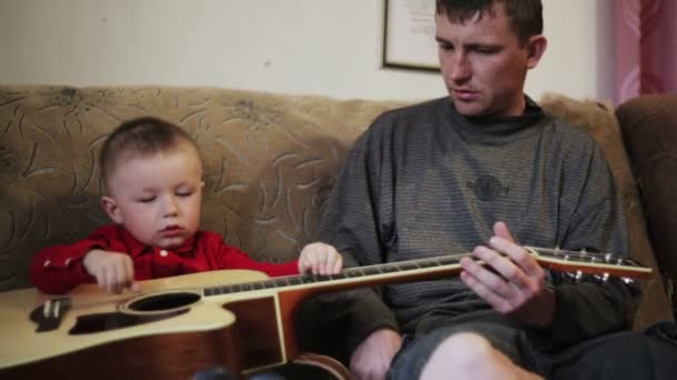 Junger Vater bringt seinem kleinen Sohn das Gitarrespielen bei — Stockvideo