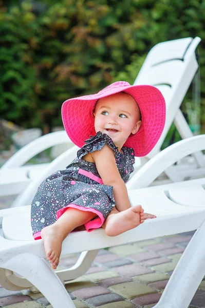 Kleines Mädchen mit rotem Hut sitzt auf einer Liege — Stockfoto