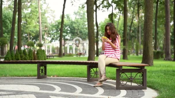 Gyönyörű nő ül egy padon a parkban — Stock videók