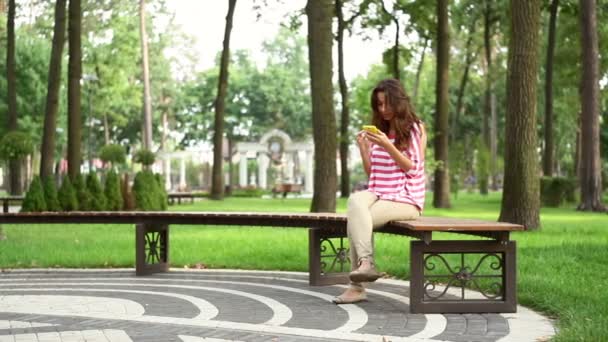 Красивая женщина сидит на скамейке в парке — стоковое видео