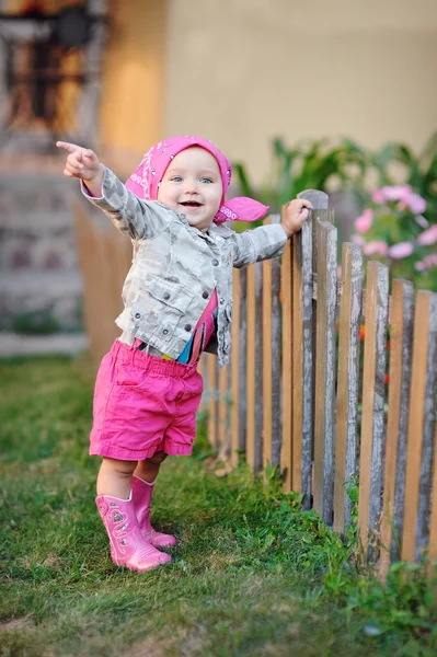 Kleines Mädchen in rosa Stiefeln am Zaun — Stockfoto