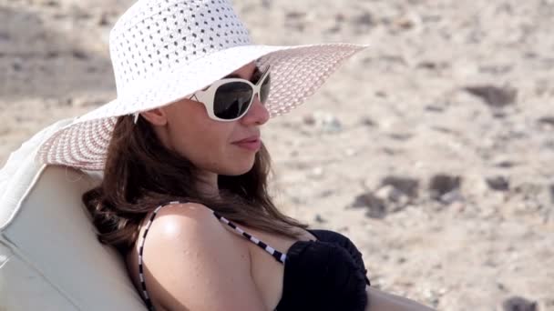 Beautiful woman in a hat and sunglasses sunbathing on the beach — Stock Video