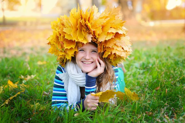 Beautiful woman in a wreath of yellow leaves lying on the grass — Stock Photo, Image