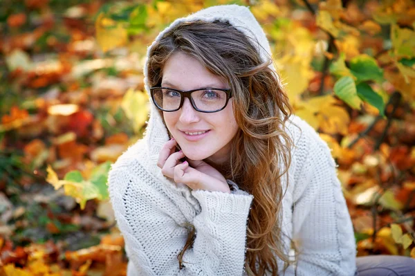 Beautiful woman in glasses sitting on yellow leaves — Stock Photo, Image