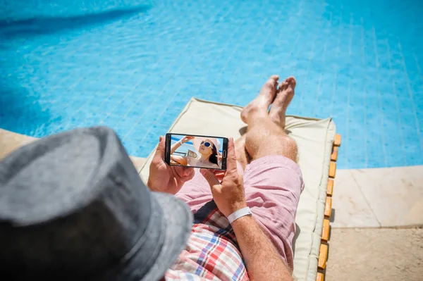 Homme au chapeau couché sur une chaise longue avec un smartphone — Photo