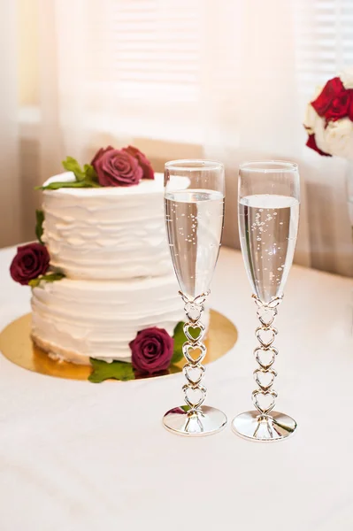 Schöner weißer Kuchen mit roten Rosen und zwei Gläsern mit Champagner — Stockfoto