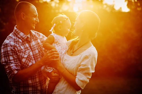 Young family with little daughter walking in the park at sunset — Stock fotografie