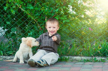 Kameraya gülümseyen sevimli küçük çocuk onun köpek yavrusu labrador ile diz çökmüş