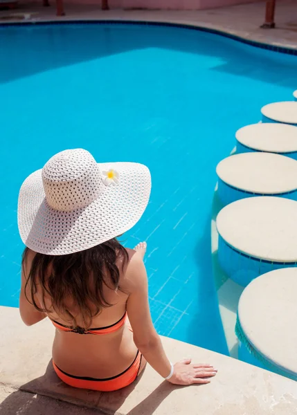 Schöne Frau genießt die Sonne und sitzt am Rande des Pools. — Stockfoto