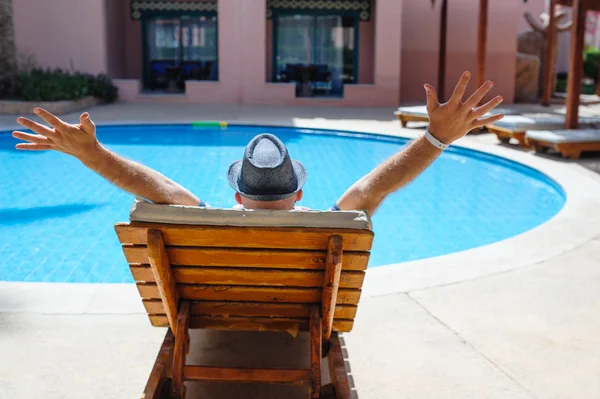 Hombre feliz con un sombrero acostado en una tumbona junto a la piscina — Foto de Stock