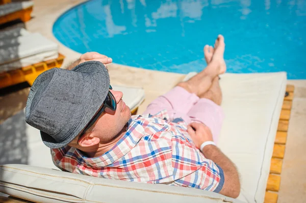 Homme heureux avec un chapeau couché sur une chaise longue près de la piscine — Photo