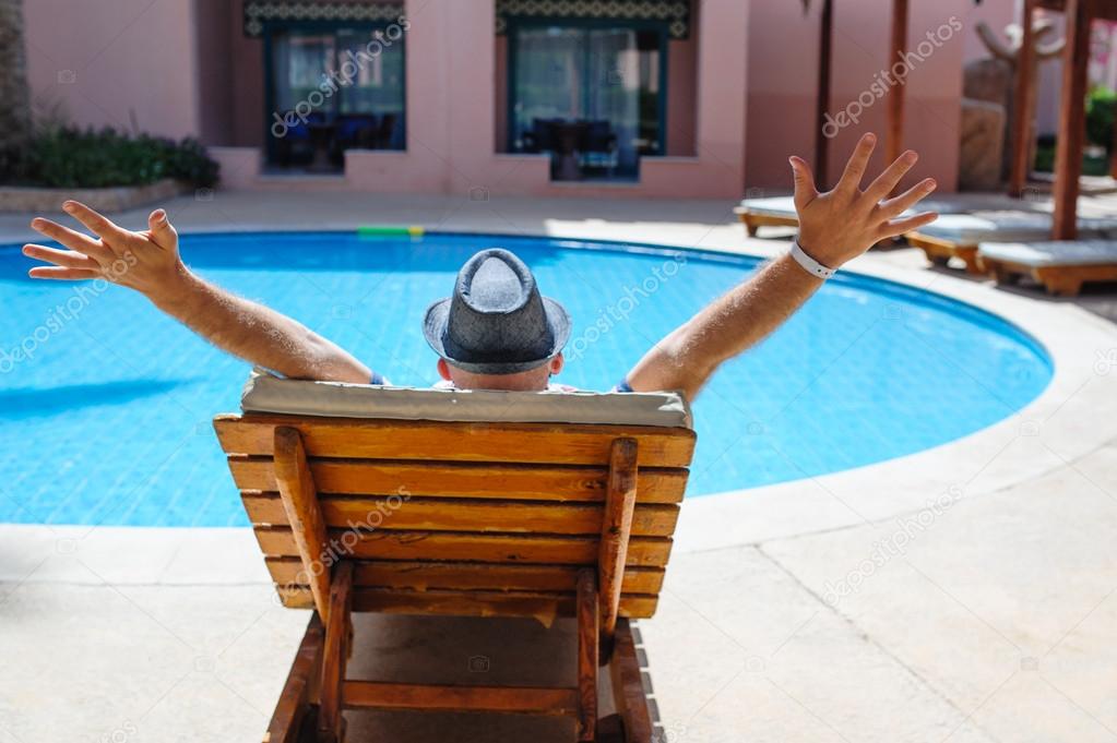 Happy man with a hat lying on a lounger by the pool