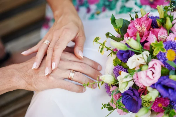 Руки нареченого і нареченого з кільцями на красивому весільному букеті — стокове фото
