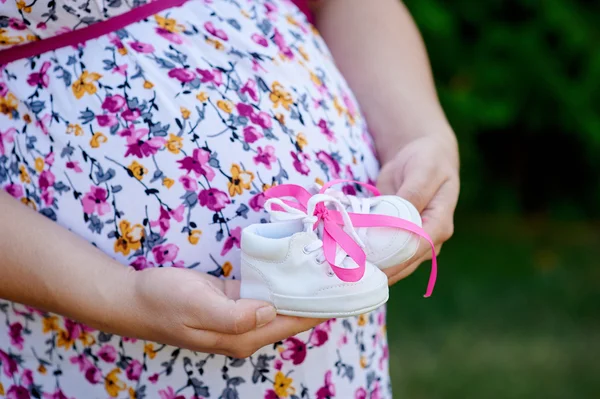 Part of pregnant woman with little shoes for baby — Stock Photo, Image