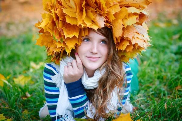 Beautiful woman with a wreath of yellow leaves lying on the grass — Stock Photo, Image