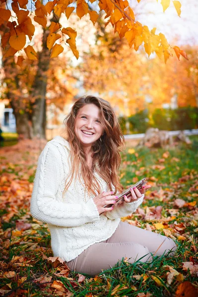 Happy woman in white blouse sitting on the grass in autumn park — Stock Photo, Image