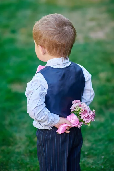 Mały chłopiec z bukietem kwiatów za jego plecami — Zdjęcie stockowe