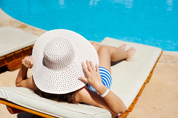 Schöne Frau mit einem großen weißen Hut auf einer Liege am Pool — Stockfoto