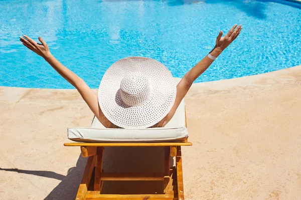 Bella donna con un grande cappello bianco su un lettino a bordo piscina — Foto Stock